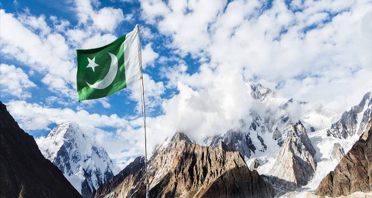 Eine pakistanische Flagge weht stolz vor einer Kulisse aus schroffen, schneegepuderten Bergen und Wolken.