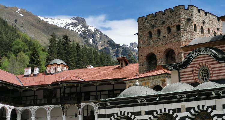 Monastère emblématique de Rila avec ses arcs rayés dressé contre les montagnes boisées et un sommet enneigé.