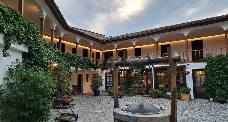 Charming courtyard of a traditional guesthouse with vine-covered walls, wooden balconies, and a hand-crank well at the center.