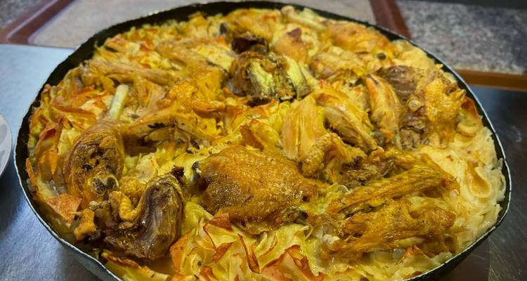 Close-up of a traditional baked dish featuring golden chicken pieces atop layers of pasta and cabbage.