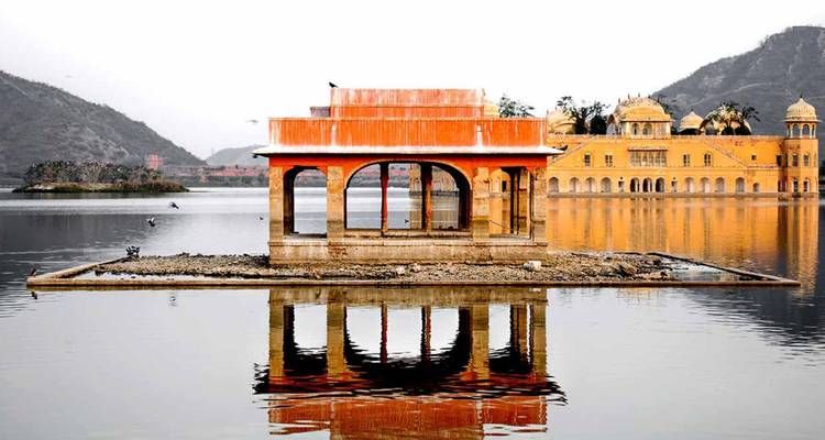 Spiegelungen des orangefarbenen Jal Mahal Pavillons und Palastes auf ruhigem Seewasser.