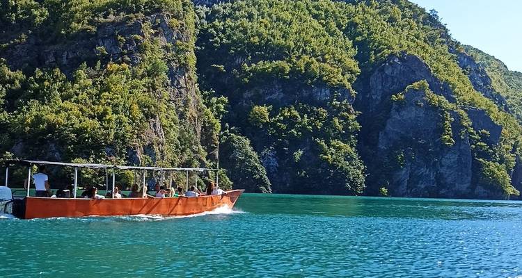 Orangefarbenes Ausflugsboot fährt durch türkisfarbene Schluchtgewässer, die von steilen grünen Klippen gesäumt sind.