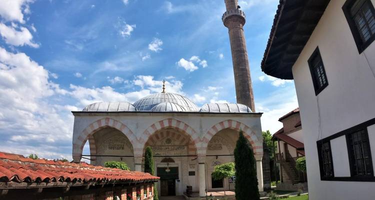 Historische Moschee aus der osmanischen Zeit mit hohem Minarett und gestreiften Bögen unter einem strahlend blauen Himmel.