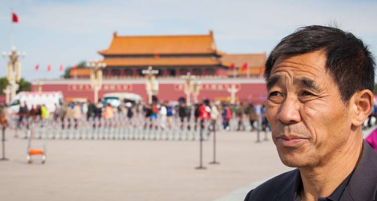 Portrait of a man with Tiananmen Gate and bustling Tiananmen Square softly blurred in the background.