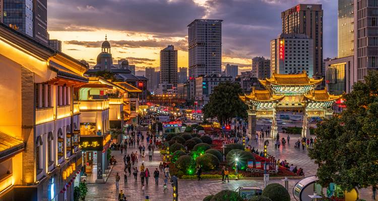 Evening cityscape with traditional gate, modern high-rises and crowds strolling brightly lit pedestrian streets at sunset.