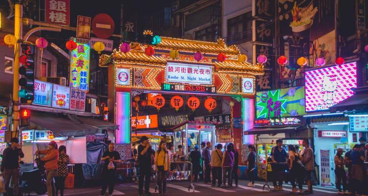Colorful entrance gate to Raohe Street Night Market glows with lanterns and LED boards as visitors gather.