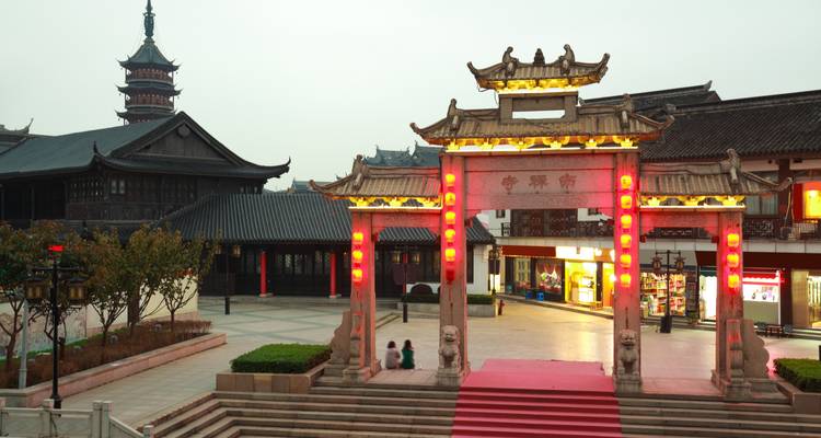 Illuminated traditional Chinese archway with red lanterns at dusk in a pedestrian plaza