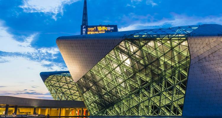 La moderna Casa de la Ópera de Guangzhou de cristal y acero brillando bajo un cielo azul crepuscular.
