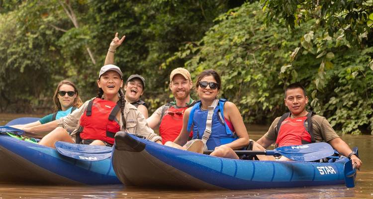 Laughing travellers sit in blue inflatable kayaks on an Amazon tributary.