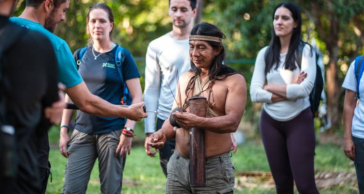 Indigenous guide demonstrates a traditional tool to visiting travellers in a clearing.
