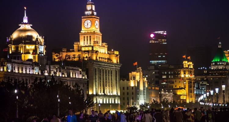 Illuminated colonial facades of Shanghai’s Bund at night with crowds strolling the waterfront promenade.