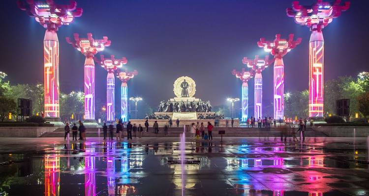 Colorful illuminated pillars and statue reflected in wet plaza at night in Xi'an’s cultural district.