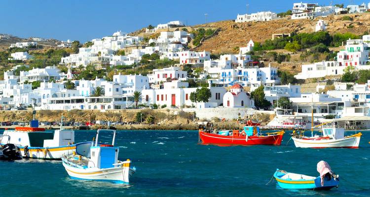 Kleurrijke vissersbootjes doberen op en neer in de levendige blauwe haven onder de witgekalkte huisjes op de helling van Mykonos.