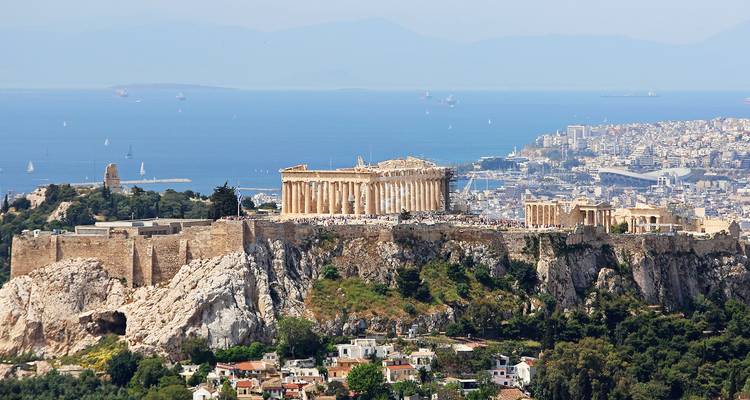 Panoramisch uitzicht op de Akropolis van Athene gelegen op een rotsachtige heuvel boven de stad met de Egeïsche Zee en zeilboten op de achtergrond.
