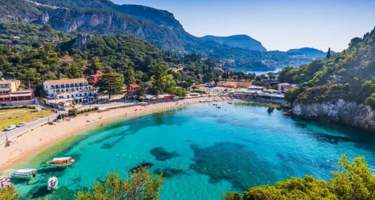 Turquoise horseshoe bay surrounded by green hills and small seaside village on Corfu island.