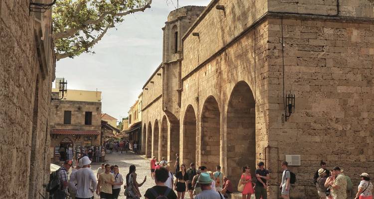 Stone-arched medieval street in Rhodes old town bustling with tourists.