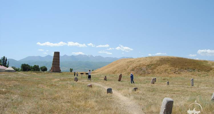Open grasveld met de oude Burana Toren en verspreide stenen balbals op de achtergrond van besneeuwde bergtoppen
