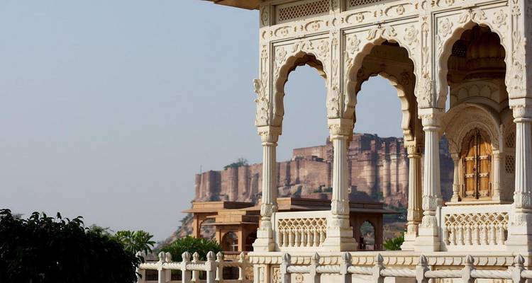 Zart geschnitzter weißer Marmorpavillon, der einen fernen Blick auf das Mehrangarh Fort auf einem felsigen Kamm einrahmt.