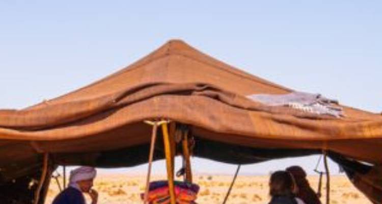 Berber tent setup in the Sahara with travelers sitting inside under clear blue sky.
