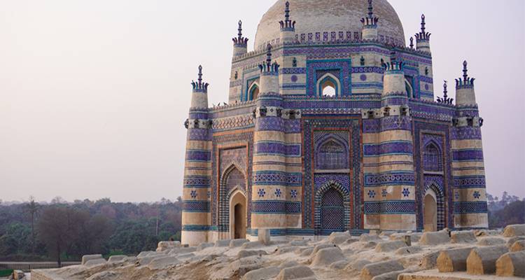Mausoleo intrincadamente decorado con azulejos, con cúpulas y minaretes que brillan suavemente al atardecer en medio de un paisaje árido.