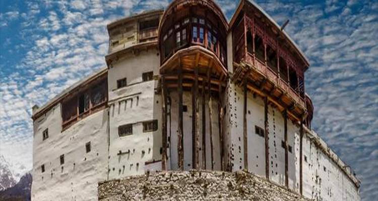 Fuerte de muros blancos desgastados encaramado en una cresta rocosa bajo un cielo dramático surcado de nubes.
