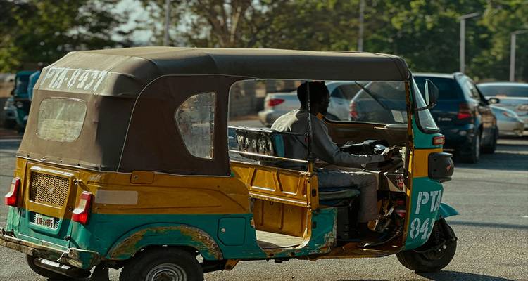 Auto-rickshaw desgastado de color verde y amarillo conduciendo por una carretera urbana concurrida a plena luz del día.