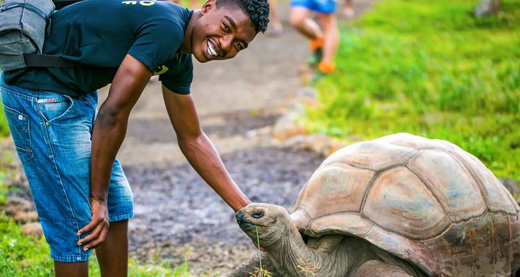 Smiling young man gently petting a giant land tortoise in a green park setting