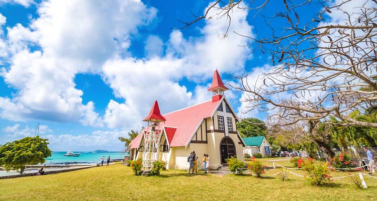 Picturesque white church with red roof near turquoise lagoon under a bright blue sky with fluffy clouds