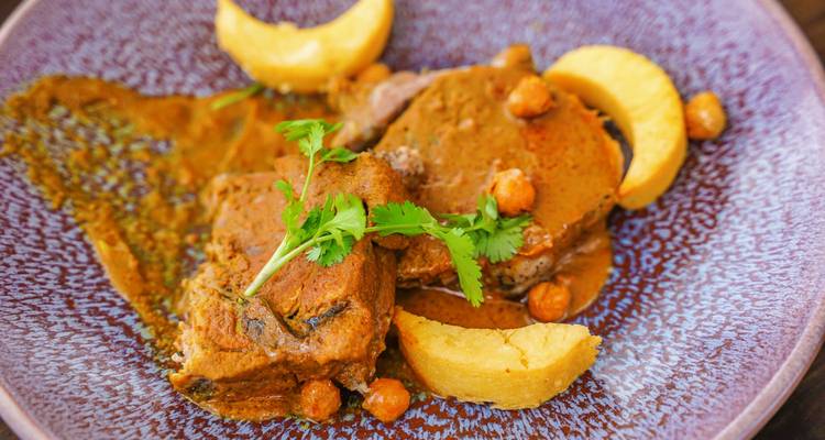 Close-up of a plated curry dish with tender meat, chickpeas, potato wedges and fresh coriander