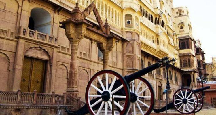 Alte Kanonen, die vor einer Sandsteinpalastmauer mit kunstvollen Balkonen und Bögen ausgestellt sind.