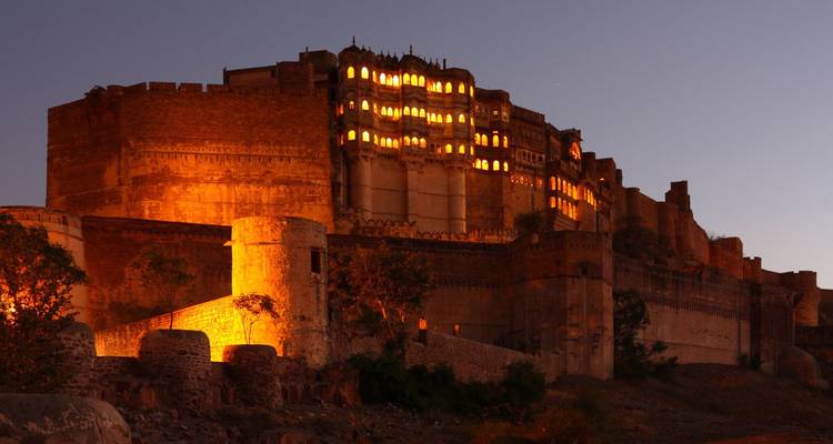 Massive Sandsteinburg, die mit warmen Lichtern gegen einen Dämmerhimmel leuchtet.