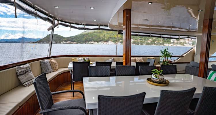 Indoor-outdoor dining space on a yacht overlooking green hills and calm water.