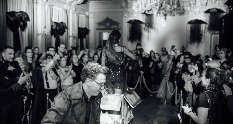 Photo en noir et blanc d'un large public regardant un spectacle sur scène dans une salle ornée.