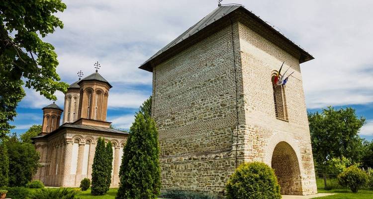 Complexe monastique historique avec tour en brique et église entourées de verdure.
