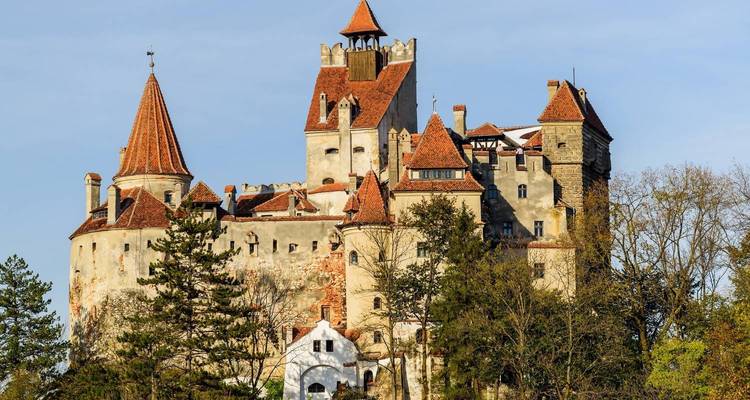 Le château de Bran s'élève au-dessus d'une colline boisée avec ses toits de tuiles rouges et ses tourelles.
