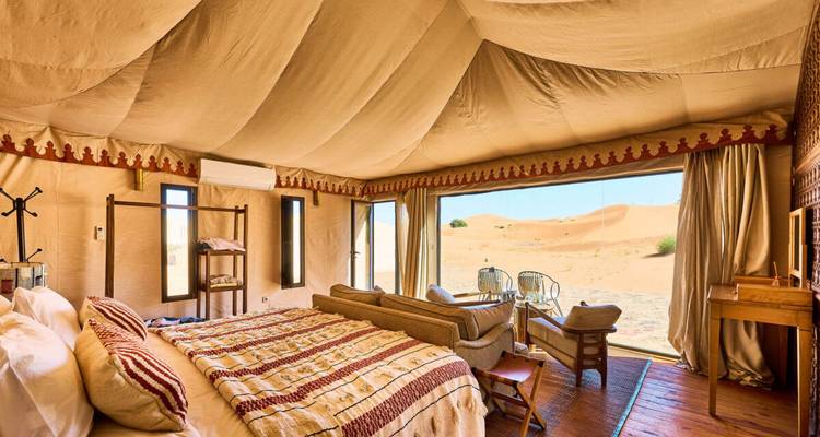 Luxuriöses Wüstenzelt-Interieur mit Kingsize-Bett, Sitzbereich und Panoramafenster mit Blick auf die Dünen.