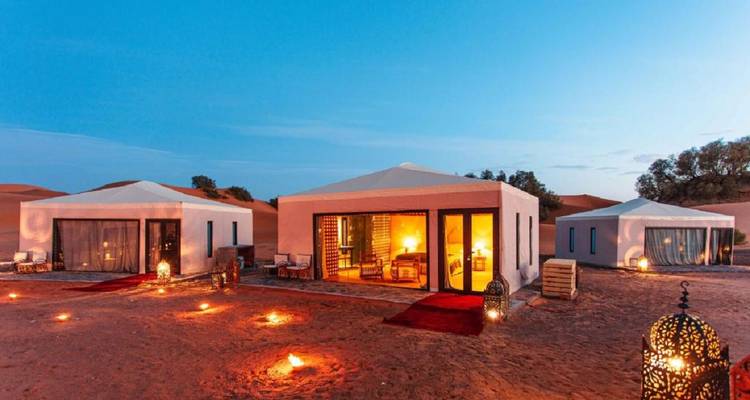 Reihe von beleuchteten Luxus-Wüstenzelten in der Dämmerung mit Laternen entlang der sandigen Wege.