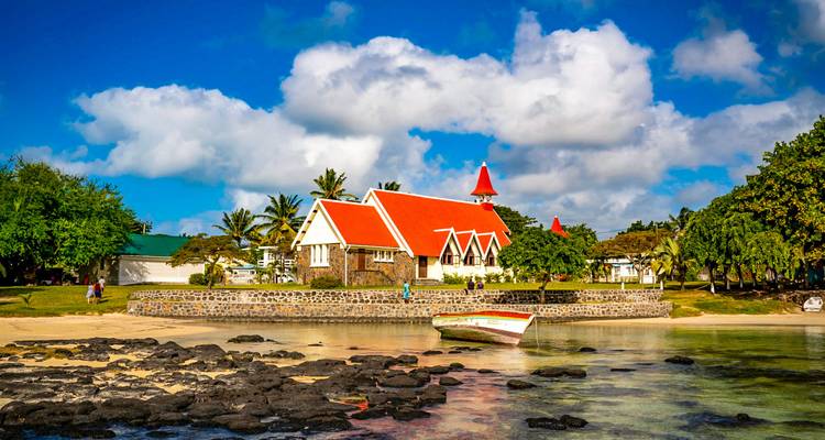 Coastal church with red roof reflected in shallow lagoon beside a small colourful boat