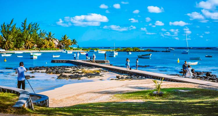 Visitors strolling on a pier and along a blue lagoon dotted with small boats and palm trees