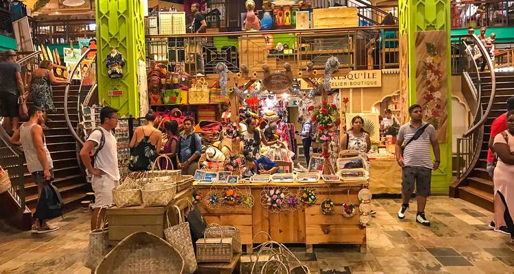 Mercado de artesanías interior abarrotado con souvenirs coloridos, cestas y compradores en piso de niveles divididos