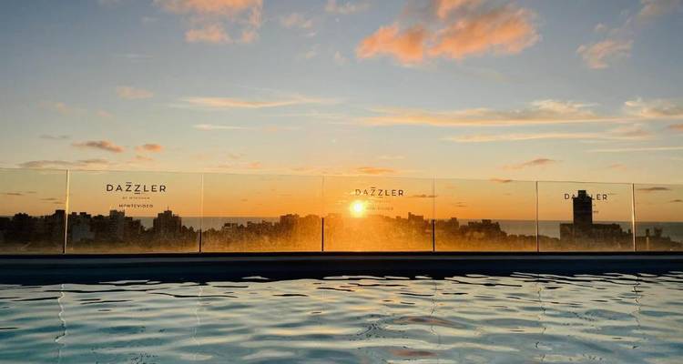 Piscine sur le toit à débordement au lever du soleil surplombant l'horizon de la ville avec la marque Dazzler sur le verre