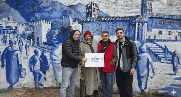 Quatre hommes posant devant une fresque aux tons bleus représentant la médina de Chefchaouen.