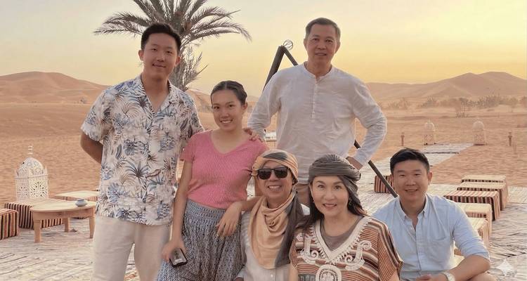 Groupe familial assis sur une plateforme de bois du désert au coucher du soleil avec de douces dunes de sable derrière.