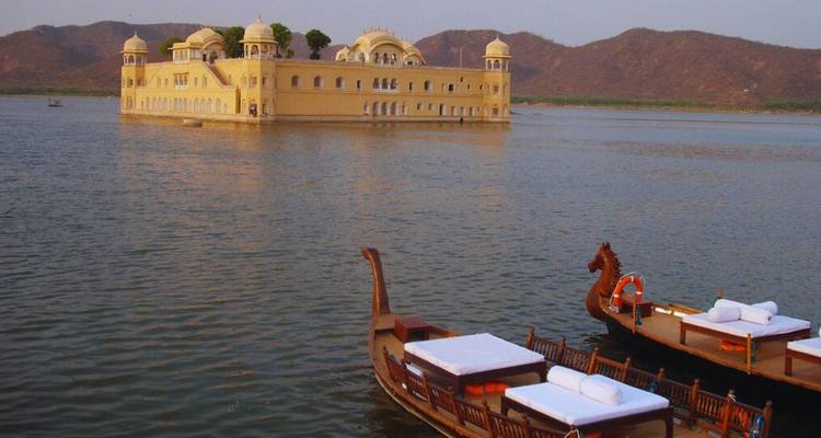 Le Jal Mahal, le palais sur l'eau, flotte sur le lac Man Sagar avec des bateaux en bois au premier plan et des collines arides en arrière-plan.