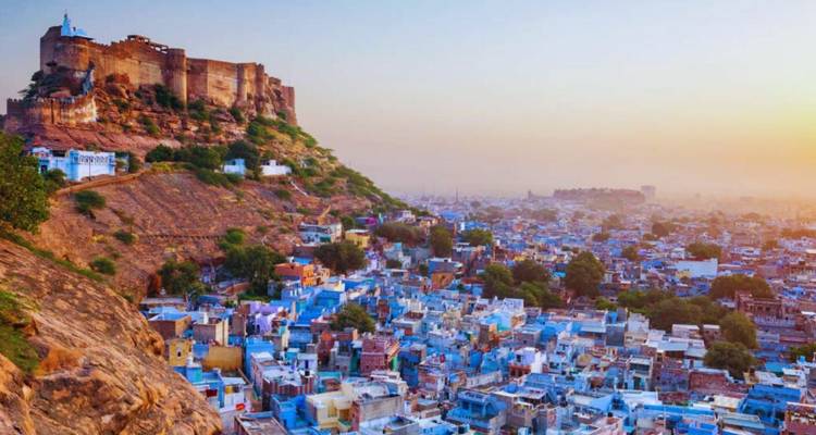 Mehrangarh Fort towering over the blue-washed houses of Jodhpur at colorful sunset.