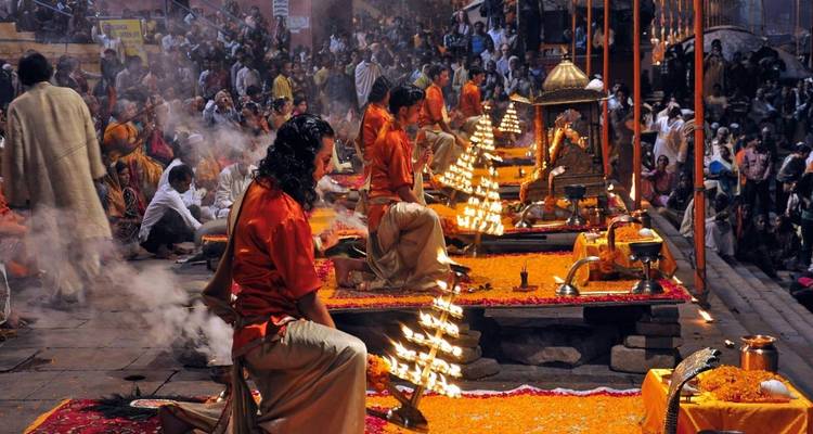 Evening Ganga Aarti ceremony in Varanasi with priests in saffron robes performing rituals surrounded by glowing lamps and crowds.