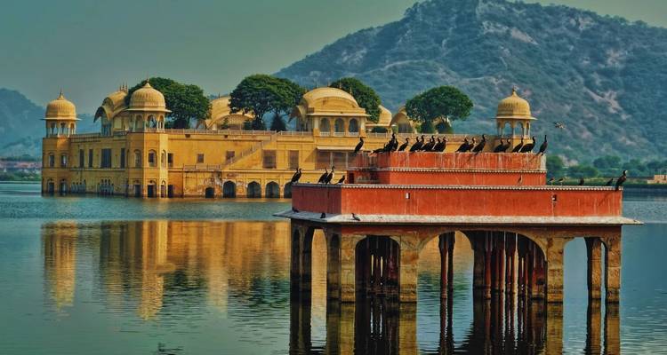 Golden Jal Mahal palace reflected in the still waters of Man Sagar Lake against a backdrop of green hills.