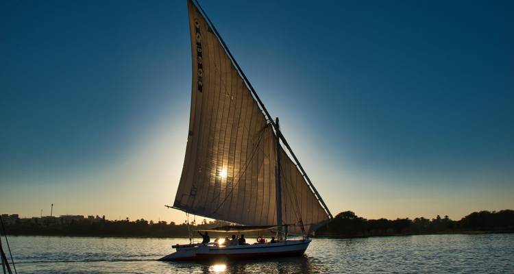 Traditional felucca sailing on the Nile at sunset, its sail glowing against the descending sun.