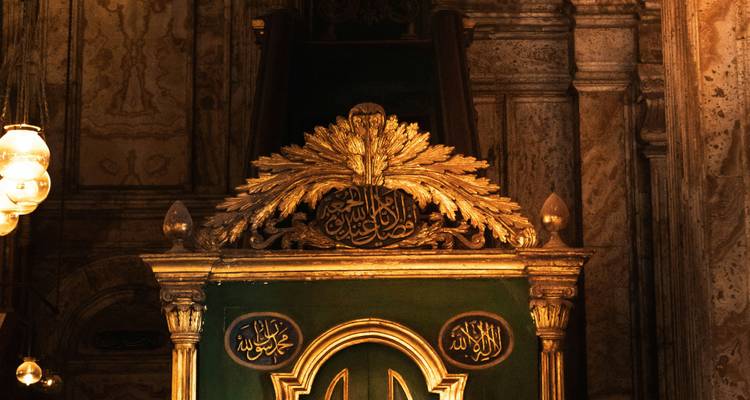 Ornate gilded calligraphy panel inside a historic Cairo mosque, warmly lit against marble walls.