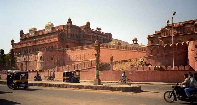 Straatbeeld van de uitgestrekte rode zandstenen vestingwerken van Junagarh Fort in Bikaner met lokaal verkeer dat voorbijrijdt.